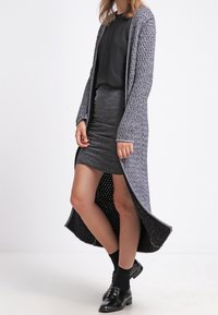 Lång, öppen cardigan i grått stickat med ett strukturerat mönster, kombinerad med en svart topp och grå pennkjol, kompletterad med svarta strumpor och skor.