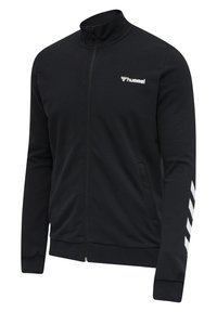Veste zippée noire avec le logo hummel blanc sur la poitrine et un motif en chevrons blancs sur la manche droite, avec des poignets et un ourlet inférieur côtelés.