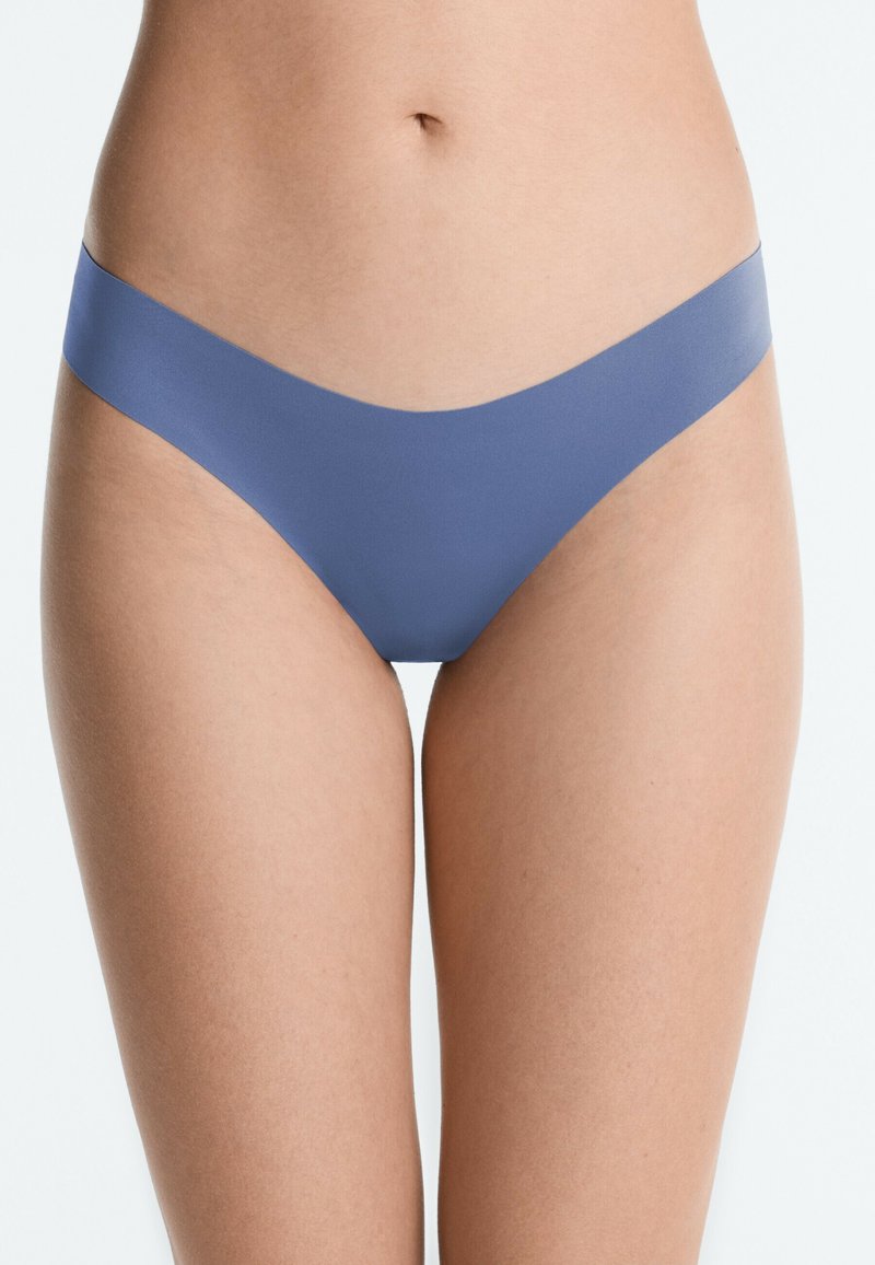 Femme portant des sous-vêtements bleus sans coutures, taille haute, montrée de la taille aux cuisses sur un fond clair.