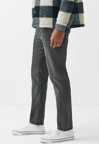 Personne portant un jean noir, des baskets montantes blanches et une veste polaire à carreaux noir et blanc, debout de profil.
