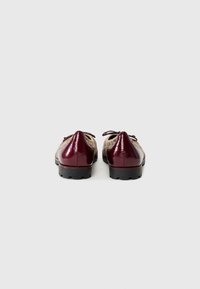 Burgundy patenttivahasta valmistetut kengät, joissa on terävä kärki, nauhakiinnitys ja teksturoitu pinta, mustalla kumipohjalla varustettu.