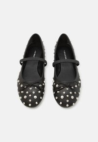 Ballerine in pelle nera con punta arrotondata, decorate con borchie argentate e un fiocco decorativo, dotate di una fascia sul dorso del piede.
