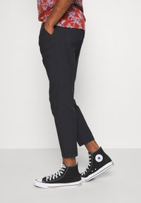 Dark navy cropped trousers with a slim fit, featuring side pockets and a smooth texture, paired with black high-top sneakers.