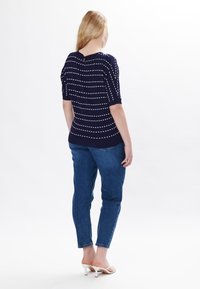 Maglietta blu navy con strisce orizzontali bianche, maniche corte e dettaglio con bottone sul retro, abbinata a jeans azzurri chiari e sandali con tacco bianchi.