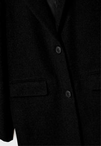 Musta villakangastakki, jossa on viiltohaalari, kaksi etutaskua ja kaksi nappia. Pehmeä rakenne klassisella muotoilulla.