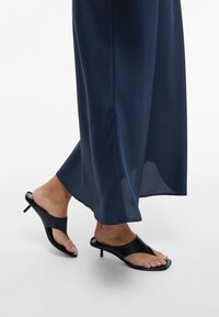 ČrneSalonke na visoki peti z obliko prstnega obročka, z sijočim usnjem in vitko peto, v kombinaciji z gladko temno modro tkanino.