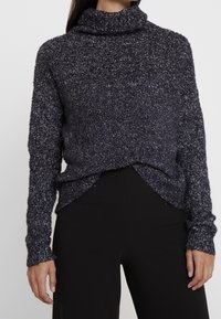 Trui met een colnek, gemaakt van gestructureerd marineblauw materiaal met lichte kleurvlekken. Heeft lange mouwen en een iets verkorte voorkant.