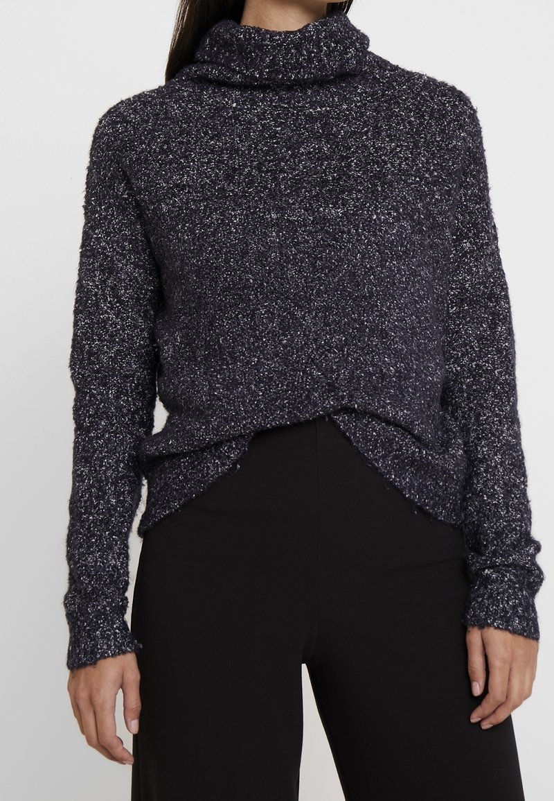 Trui met een colnek, gemaakt van gestructureerd marineblauw materiaal met lichte kleurvlekken. Heeft lange mouwen en een iets verkorte voorkant.