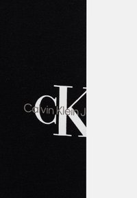 Svart bomullstyg med stora vita bokstäver som säger "CK" och "Calvin Klein" i grått. Texturen är slät och enhetlig.