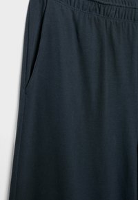 Pantalones deportivos azul oscuro con cinturilla elástica, bolsillos laterales y textura suave de algodón. Presentan un diseño de pierna cónica.