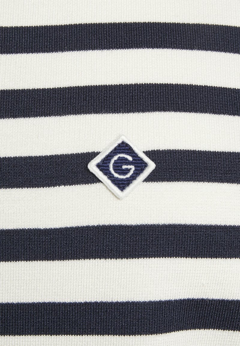 Niebiesko-biały dzianinowy materiał w paski z diamentowym naszywką z białym logo "G". Teksturalny, dopasowany krój z poziomymi paskami.