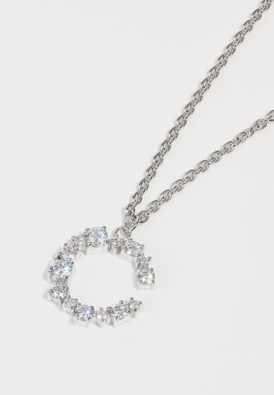 Ασημένιο κολιέ με ανοιχτό κυκλικό μενταγιόν διακοσμημένο με πολλαπλά διάφανα πετράδια, αναδεικνύοντας τη σύγκρουση ανάμεσα στο λείο μέταλλο και τις λαμπερές πέτρες.