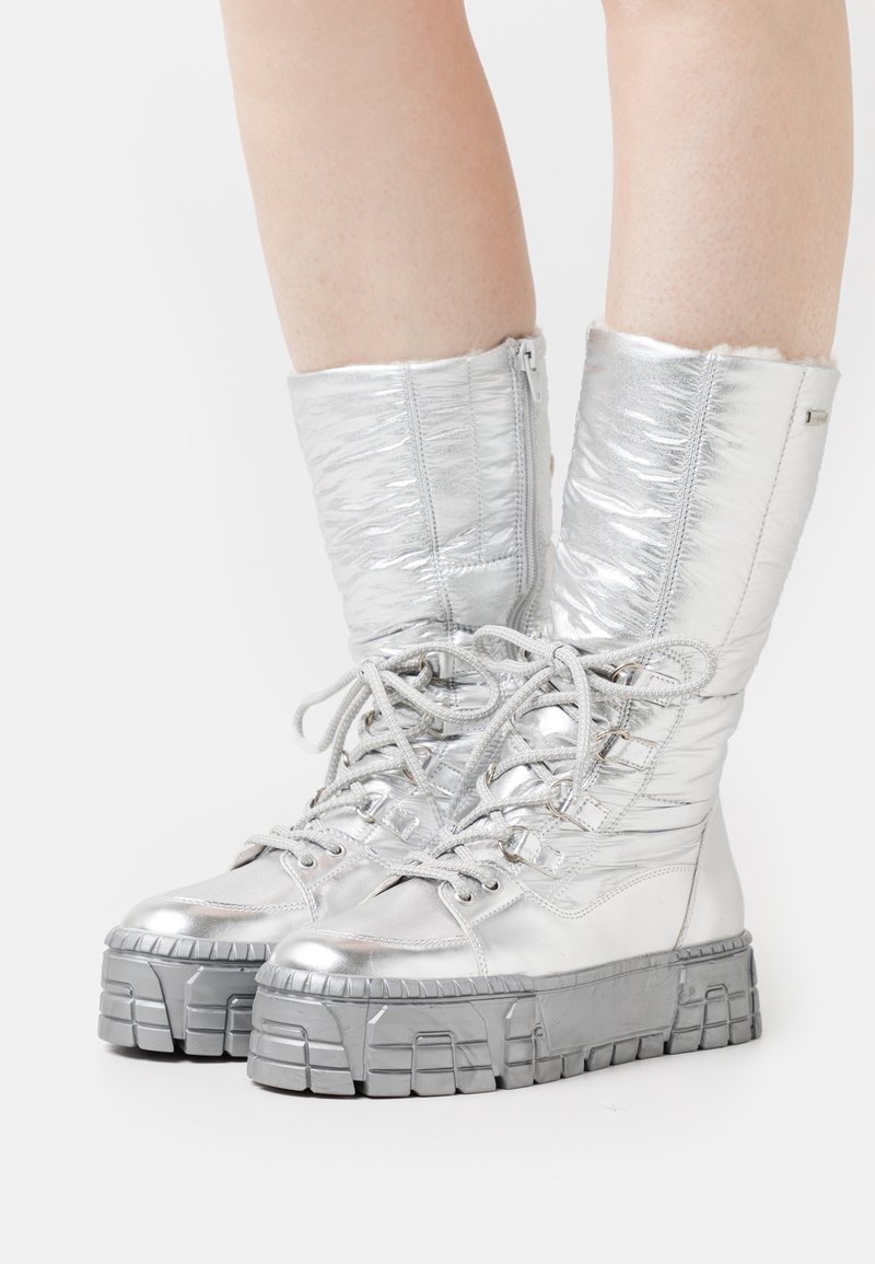 Botas plateadas metálicas con textura acolchada, caña alta y diseño de cordones. Suelas de goma gris gruesas con detalles estriados. Cierre lateral con cremallera.