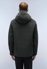 Giacca in pile grigia scura con cappuccio, caratterizzata da una superficie testurizzata e un design semplice, indossata da una persona vista di spalle.