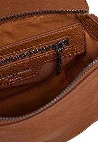 Inneres einer braunen Lederhandtasche, das eine mit einem schwarzen Reißverschluss ausgestattete Tasche sowie ein gesticktes Markenlabel auf dem Stofffutter zeigt.