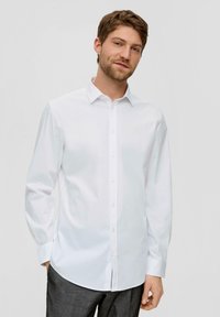 Camicia bianca a maniche lunghe con colletto button-down, realizzata in tessuto morbido. Presenta un taglio dritto e bottoni lungo la pattina anteriore.