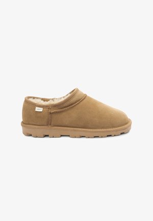 Chaussure slip-on en suède marron avec une doublure en fausse fourrure douce, un design à profil bas et une semelle en caoutchouc texturé. Étiquette de marque visible sur le côté.