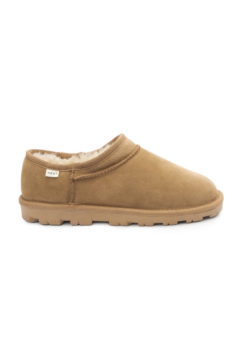 Brun, ruskind slip-on sko med blød, kunstpelsforing, lavprofil design og en tekstureret gummisål. Brandingmærke synligt på siden.