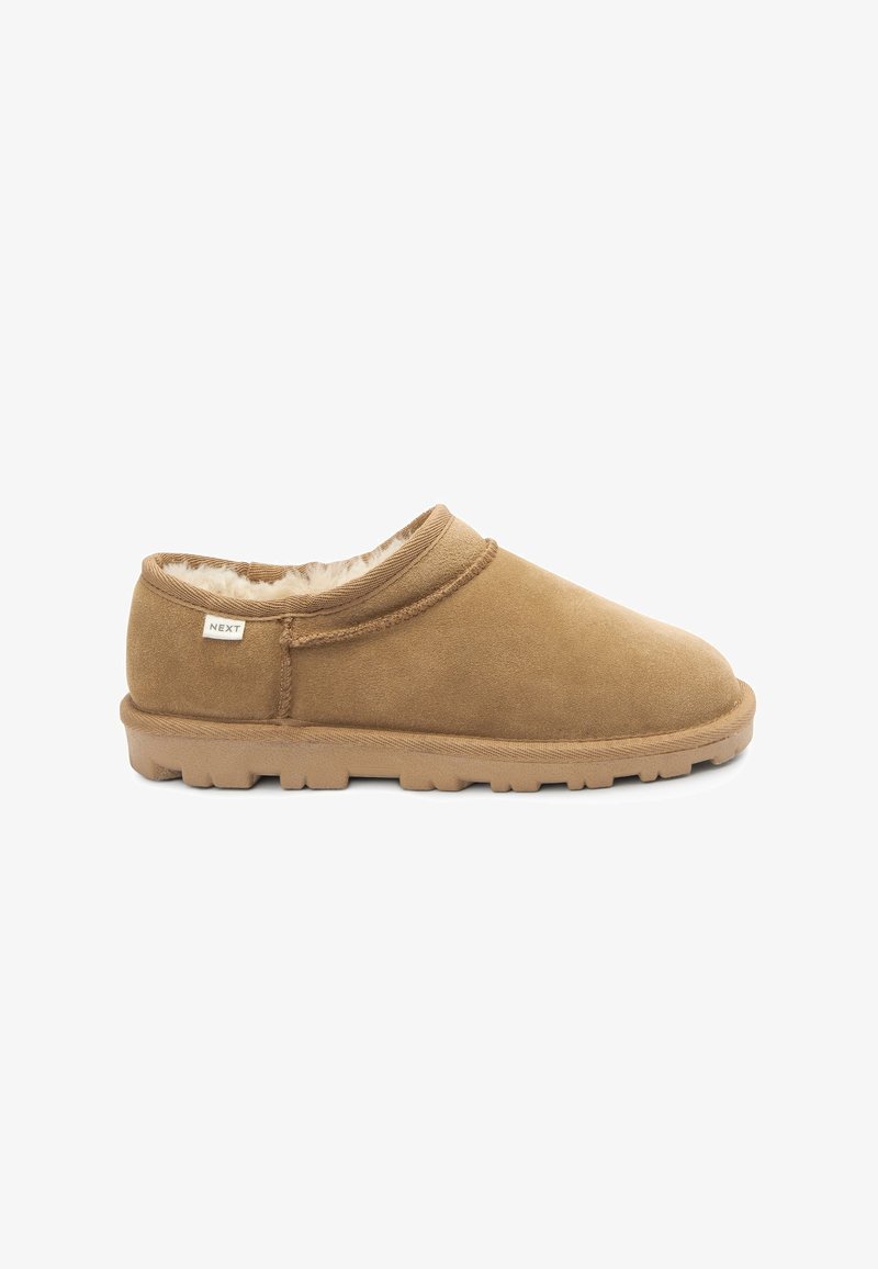 Chaussure slip-on en suède marron avec une doublure en fausse fourrure douce, un design à profil bas et une semelle en caoutchouc texturé. Étiquette de marque visible sur le côté.