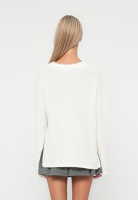 Pull blanc à manches longues en tricot doux et texturé ; présente une coupe décontractée, un col rond et un ourlet arrière légèrement plus long.