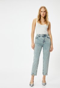 Ljusblå, högmidjade jeans med rak passform, som har en något urtvättad textur och framklippt i nederkant, parat med en vit linne.