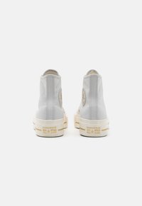 Szare wysokie trampki z płótna z kremowymi gumowymi podeszwami. Posiadają okrągłe logo oraz napis "CONVERSE ALL STAR" na pięcie.