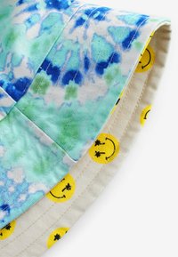 Stripet bøttehat med et tie-dye mønster i blå og grøn. Indersiden har et smiley-ansigt mønster på en beige baggrund.