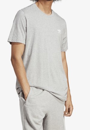 Grijze katoenen t-shirt met korte mouwen, ronde halslijn en een klein wit logo op de linkerborst. Casual pasvorm, gecombineerd met grijze joggers.