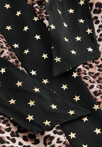 Tessuto nero con motivo di stelle dorate insieme a stampa leopardata, evidenziando texture e design contrastanti, adatto per abbigliamento alla moda.