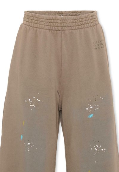 Pantaloni della tuta color taupe con vita elastica, caratterizzati da piccole macchie di vernice bianca, stampe di foglie blu e un timbro numerato sulla coscia destra.