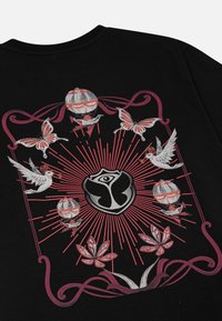 Zwarte T-shirt met een centraal logo, omringd door rode stralen, vlinders, duiven en luchtballonnen in gedetailleerde witte en rode illustraties.