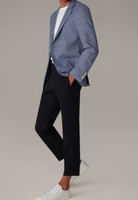 Niebieska marynarka w kratę gingham z wyciętym kołnierzem, noszona na białym t-shircie, w połączeniu z czarnymi spodniami i białymi tenisówkami, prezentująca nowoczesny krój.