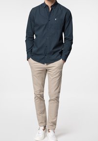 Marinfärgad skjorta med vita prickar, tillsammans med ljusbeige byxor och vita sneakers. Fokusera på en skräddarsydd passform och en avslappnad stil.