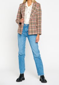 Kratkowana marynarka w kolorach różowym, czarnym i kremowym, o dopasowanym kroju, z klapami o notchach, noszona na białej koszuli, zestawiona z niebieskimi dżinsami i czarnymi botkami.