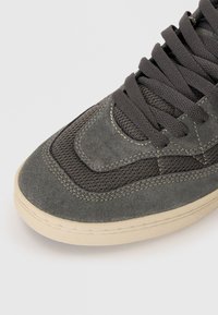 Gray suede and mesh sneaker upper, featuring dark gray laces, a textured design, and a cream rubber sole with subtle stitching details.