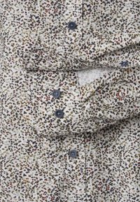 Short-sleeve shirt in lightweight fabric with a white base and brown, green, and red speckled pattern; features gray buttons and folded cuffs.