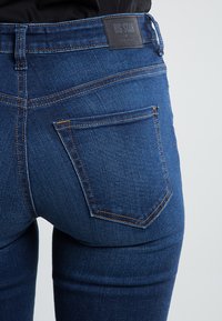 Jeans de mezclilla azul con un ajuste ceñido, que presentan un pequeño bolsillo trasero y costuras claras. La cinturilla tiene una etiqueta negra "BIG STAR".
