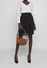 Sac à main en simili cuir marron à motif serpent avec une chaîne dorée, associé à un haut gris à manches longues en col en V et une jupe plissée noire.