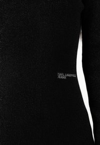 Must mustriga kangast top, millel on õrn sära, valge külgdetailiga. Seal on logo silt, millel on kirjas "KARL LAGERFELD JEANS."