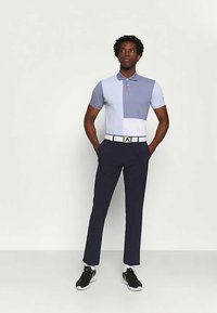 Muška polo majica s dizajnom u bojama svijetloplave i bijele. Uparena s tamnoplavim hlačama i bijelim remenom. Tenisice upotpunjuju izgled.