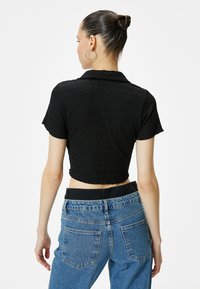 Sort cropped top med en struktureret, rynket stof og kortærmede, parret med højtaljede blå denim jeans med to baglommer.