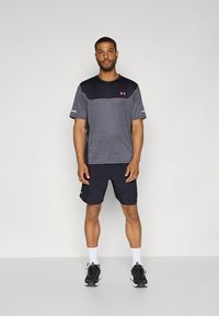 Mörkgrå atletisk t-shirt med ljusgrå horisontell rand, kombinerad med marinblå shorts. Har Under Armour-logotyp i rosa, med svarta sneakers.