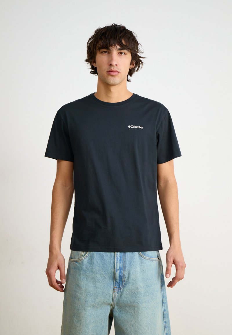 Svart bomull T-skjorte med korte ermer, rund hals og hvit Columbia-logo på venstre bryst. Bært med lyse denimshorts.