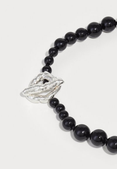 Μαύρο κολιέ με χάντρες που διαθέτει γυαλιστερές μαύρες χάντρες και μία υφασμένη ασημένια κλείσιμο με οργανικό, σπειροειδή σχέδιο.