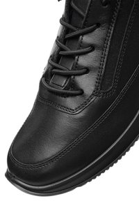 Schwarze Ledersneaker mit detaillierter Naht, schwarzen Schnürsenkeln und einer strukturierten Sohle, sichtbar vor einem weißen Hintergrund.