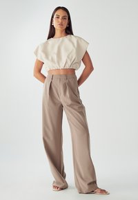 Top beige accorciato con vita arricciata; pantaloni taupe a vita alta e gamba larga; tessuto liscio con dettagli minimi; modella in piedi.