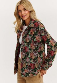 Kurtka w kwiatowy wzór w ciemnozielonym kolorze, z odcieniami czerwonych i różowych róż, z kołnierzykiem i dwoma kieszeniami na piersi.