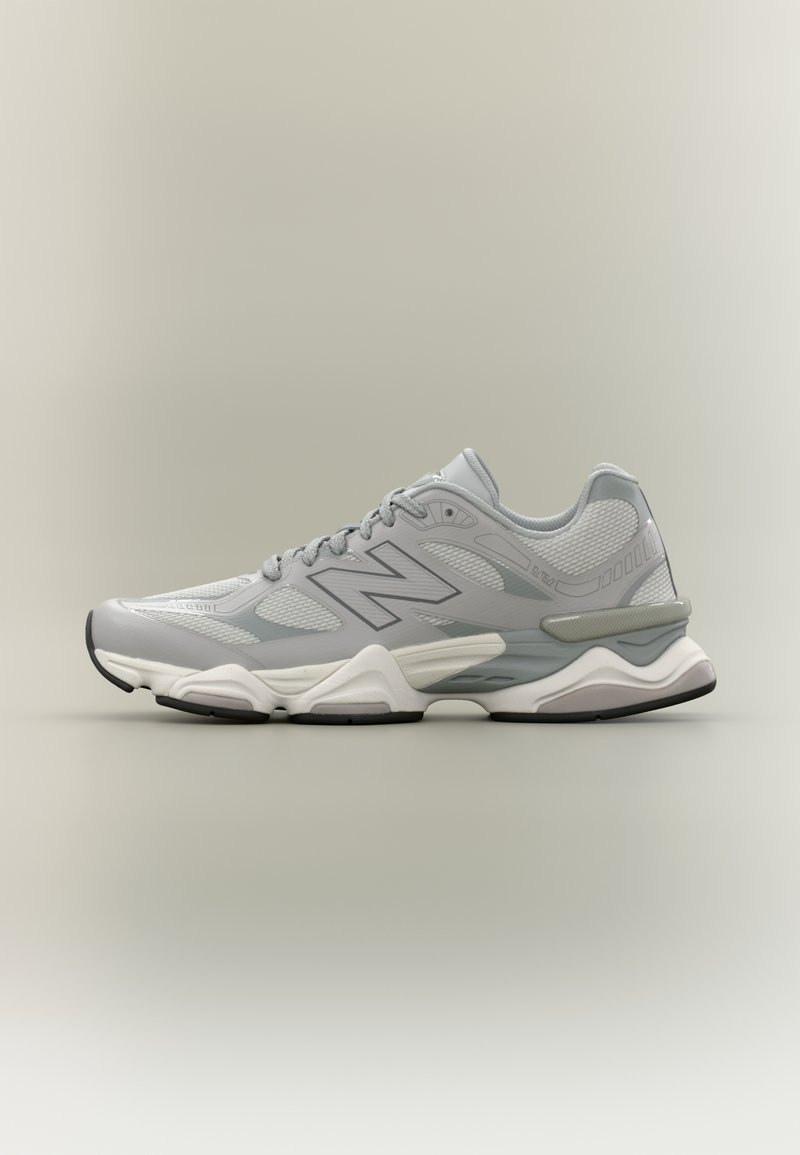 Baskets de sport grises et blanches avec tige en mesh et synthétique, design à lacets, semelle rembourrée et logo de marque latéral sur fond neutre.
