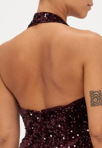 Vestido de lentejuelas color burdeos con diseño de cuello halter. Presenta un corpiño ajustado y cierre de cremallera en la parte trasera. La espalda está descubierta con una textura de piel suave.