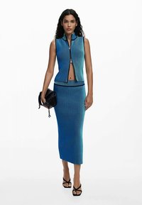 Dvoslojni pleteni komplet u plavim nijansama, uključujući top bez rukava sa patentnim zatvaračem i dugu prigodno krojenu suknju s horizontalnim rebrastim detaljima.